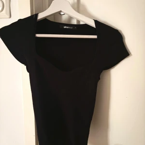 Svart ribbad topp från Gina Tricot - En svart ribbad topp från Gina Tricot med fyrkantig urringning och korta ärmar. Snygg och enkel modell som är lätt att matcha till olika outfits. Materialet är stretchigt och sitter snyggt på kroppen.