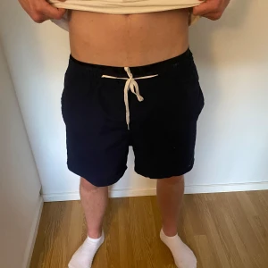 Mörkblå badshorts  från Tommy Hilfiger - Snygga mörkblå badshorts från Tommy Hilfiger med vit snörning i midjan och diskret logga på benet. Perfekt nu till sommaren! Sparsamt använda och i mycket bra skick.