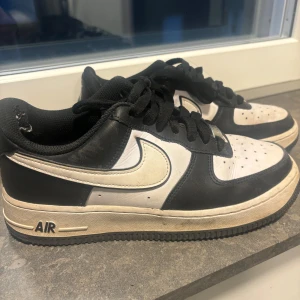 Nike Air Force 1 svartvita sneakers - Svartvita Nike Air Force 1 sneakers med klassisk låg siluett. Skorna har svart ovandel i skinn med vita paneler och vit swoosh, svart snörning och vit sula med svart yttersula. Perfekta för dig som gillar streetstyle och tidlös design. Dom andvända ganska mke därav priset då dem har ”hål” i båda vid hälen men går  fixar med klistermärket från Clas Olsson 😊