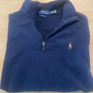 Estate rib quarter zip Polo Ralph Lauren - Snygg marinblå tröja från Polo Ralph Lauren med half zip och klassisk broderad logga på bröstet. Tröjan är ribbad och har hög krage! Otroligt fin med en skjorta under eller en basic T-shirt 