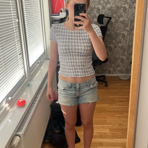 Rutig topp från Zara - Croppad topp från Zara i vitt och blått rutigt mönster. T-shirten har korta ärmar med vågig kant och är gjord i ett stretchigt material.
