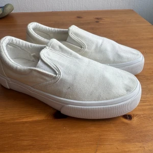 157 Vita Slip-on Skor Storlek 37 - Ett par vita slip-on skor. Perfekta för en avslappnad stil. Bekväma och lätta att ta på och av.