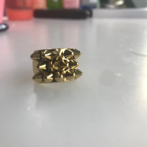 Peak Ring från Edblad - (Säljs pga att den är för stor och det går för länge för att byta storlek. Aldrig använd, endast testad) Cool statementring i guld med flera spetsiga nitar framtill. Ringen har en bred design och är tillverkad i metall med blank finish. Perfekt för dig som vill sticka ut och addera lite edge till din stil.