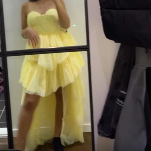 Gul volangklänning med hjärtformad urringning - Supersöt gul klänning med hjärtformad urringning och flera lager volanger. Klänningen är längre bak och kortare fram, vilket ger en cool high-low effekt. Ärmlös och perfekt för dig som vill sticka ut med en riktigt drömmig look.