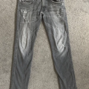 Replay Anbass grå jeans med slitningar - Snygga Replay Anbass jeans i grå tvätt med slitna detaljer på låren och knäna. Klassisk femficksmodell med svarta broderier på bakfickorna och logopatch i skinn. Jeansen har rak passform och är tillverkade i mjukt jeanstyg. Inga defekter över huvud taget! Priset kan diskuteras vid snabb affär!.