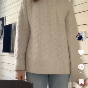 Beige kabelstickad tröja - Säljer en chunky krämvit kabelstickad tröja med hög hals och långa ärmar. Tröjan har ett klassiskt flätmönster framtill och ribbade muddar vid ärmslut och nederkant. Perfekt för lager-på-lager och riktigt mysig under kyliga dagar. Etiketten säger XS men skulle säga att det är en S. Endast använd fåtal gånger. 