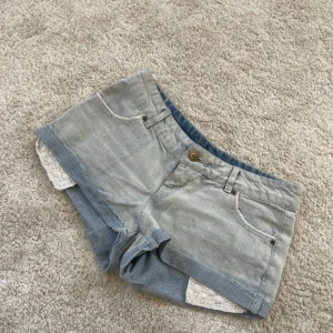Ljusblå jeansshorts med spets Calzedonia - Supersnygga ljusblå jeansshorts från Calzedonia med coola bakfickor och vit virkad spets som sticker fram nedtill. Klassisk femficksmodell med knapp och dragkedja. Perfekta shorts för sommaren som ger unika detaljer till din outfit. Mått: midjemått: ca 40cm. Midjehöjd: ca 18cm. Lårmått runtom: ca 61cm. Mycket bra skick, förutom knappen som sitter lite löst. 