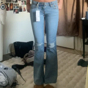Ljusblå bootcut jeans med slitningar - Säljer ett par ljusblå bootcut jeans från Ginatricot med snygga slitningar vid knäna och detaljerade bakfickor med lock och knappar. Dem är sprillans nya och jag säljer dem då dem är för små 