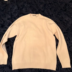 Beige stickad tröja från Zara - En stilren beige stickad tröja från Zara i storlek S. Tröjan har rund halsringning, ribbade muddar och är långärmad. Perfekt för lager-på-lager och enkel att matcha med jeans eller kjol.