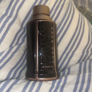 Hugo Boss The Scent Le Parfum 100ml - Säljer en Hugo Boss The Scent Le Parfum i 100 ml flaska. Flaskan är mörkbrun med bronsfärgade detaljer och har en robust, maskulin design med BOSS-loggan i relief. Perfekt för dig som gillar eleganta och kraftfulla dofter.