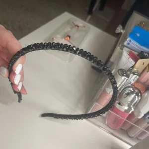Svart diadem med glittriga stenar - Snyggt svart diadem dekorerat med små glittriga stenar som ger en extra touch till din look. Perfekt accessoar för att lyfta vilken outfit som helst med lite extra bling. Smal och stilren design som sitter bekvämt på huvudet.