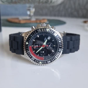 Svart kronografklocka från Invicta - Sportig kronografklocka från Invicta med svart urtavla, röda och gröna detaljer samt datumvisning. Boetten är i silverfärgat rostfritt stål och armbandet är svart och robust. Klockan har tydliga index, vridbar bezel och flera små urtavlor för extra funktioner.