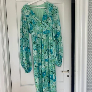 Blommig långklänning i grönt och blått - Långklänning med blommigt mönster i gröna och blå toner. Väldigt bra skick, använd en gång men sitter för tajt på mig. Storlek 36💚