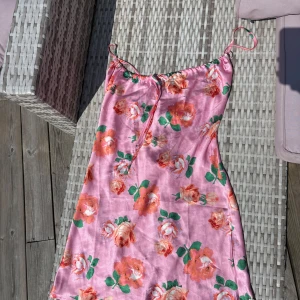 Rosa blommig sommarklänning - Rosa kort klänning med röda blommor från asos, dock ingen lapp kvar. Klänningen passar mig som är s/m och är 164 cm lång men kan även passa större. Använd en midsommar!