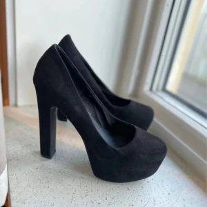 Svarta mockapumps från H&M Divided - Snygga svarta pumps i mockaimitation från H&M Divided. Skorna har hög klack och plattform för extra höjd och stabilitet. Rund tå och klassisk siluett som ger en stilren look. Perfekta för dig som vill sticka ut med en edgy vibe.