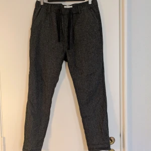 Mörkgrå byxor i ullblanding - Mörkgrå byxor med dragsko i midjan och avsmalnande ben. Byxorna är gjorda i en ullmix med viskos och polyester, vilket ger ett stilrent och en snygg look. 
