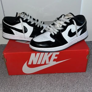 Nike Air Jordan 1 Low SE Concord svart/vit - Nike Air Jordan 1 Low i svart och vitt med klassisk Jordan Wings-logga på hälen. Skorna har snörning, vit mellansula och svart yttersula. Ovandelen är i blankt skinn och mesh, med perforerad tåbox för extra ventilation. Perfekta för dig som gillar streetstyle. Använd under 5 ggr