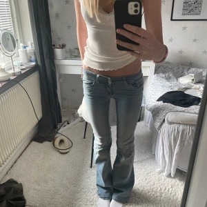 Ljusblå bootcut jeans med brodyr - Säljer ett par ljusblå bootcut jeans med låg midja och snygg rosa brodyr på bakfickorna. Jeansen har klassisk femficksmodell och är i mjukt denimtyg.