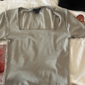 Ljusgrå topp med fyrkantig ringning Amisu - Snygg ljusgrå topp från Amisu med korta ärmar och trendig fyrkantig ringning. Toppens stilrena design gör den enkel att matcha och den är tillverkad i mjuk bomullsblandning för en skön känsla. Perfekt för dig som gillar minimalistiska plagg med modern touch.