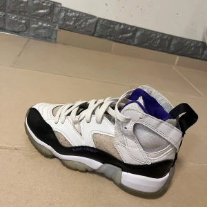 Nike Jordan jumpman two trey - Nike Jordan 1 Retro sneakers med vit och svart ovandel, lila detaljer och klassisk Jumpman-logga. Skorna har snörning, hög siluett och en robust platt sula. Materialmix av skinn och syntet, med ventilerande mesh vid tungan och vadderad krage för extra komfort.