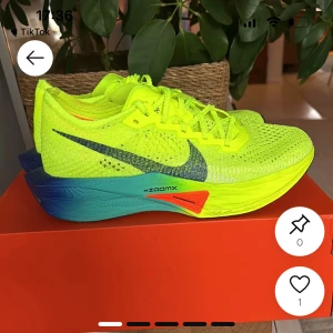 Nike löparskor i neon och blått - Nike löparskor i neon-gult med stickad ovandel och svart swoosh. Sulan är färgad i blått, grönt och orange med ZoomX-dämpning. Skorna har snörning och en sportig, modern look som sticker ut.