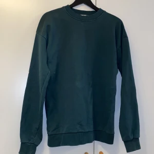 Mörkgrön sweatshirt från NA-KD - Enkel och stilren mörkgrön sweatshirt från NA-KD i storlek XS. Tröjan har rund halsringning, långa ärmar och ribbade muddar vid ärmslut och nederkant. Perfekt för en chill och avslappnad look.