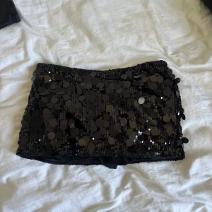 Svart paljettkjol i kort modell - Supersnygg svart kortkjol täckt med stora glittrande paljetter. Kjolen har en tight passform och är fodrad på insidan för extra komfort. Aldrig använd💕