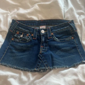 True Religion jeanskjol med rå kant - Snygga mörkblå jeanskjol från True Religion med rå, fransig kant och klassiska kontrastsömmar. I storlek 25 och saknar knappar där bak