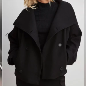 Svart kappa as najs kappa från mald - Nypris 999kr. Snygg svart kappa med bred krage och dubbelknäppning. Jackan är croppad och har en loose passform med långa ärmar. Tillverkad i ullblandning som ger en stilren och clean look. Perfekt för dig som gillar minimalistisk stil.