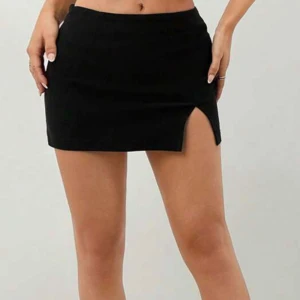 Svart minikjol med slits - En svart, tight minikjol med en snygg slits framtill. Kjolen har en enkel och stilren design som sitter högt i midjan och ger en clean look. Perfekt för dig som gillar minimalistiska plagg med en liten twist. Kan även passa som xs