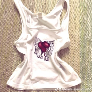 Vit linnetopp med hjärtmotiv H&M XS - Säljer en vit linnetopp från H&M i storlek XS. Toppen har ett tryck (egengjort) med ett rött hjärta med vingar och en säkerhetsnål, samt droppande detalj. Modellen är ärmlös och har en klassisk racerback. Perfekt för dig som gillar edgy och unik stil. Trycket är gjort med alcoholpennor så den bör tvättas försiktigt men det borde inte gå bort