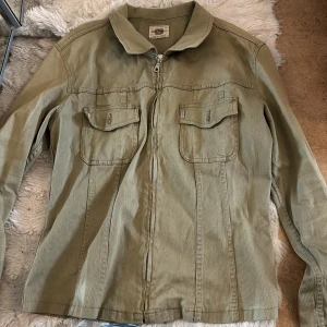 Olivgrön jacka med dragkedja - Snygg olivgrön jacka från FLASH i manchester med dragkedja framtill och två bröstfickor med lock. Klassisk krage och raka linjer ger en clean look. Ser ingen storlek men den kanske är i typ S😁