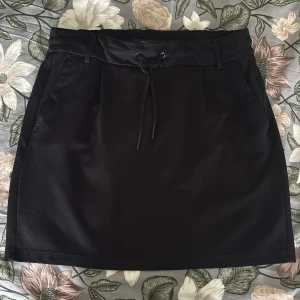 Kjol - Svart kortkjol från ONLY med dragsko i midjan och bälteshällor. Kjolen har en enkel, stilren design och är perfekt för dig som gillar en clean look. Materialet känns mjukt och lätt, och passformen är normal. Skriv vid frågor🤩