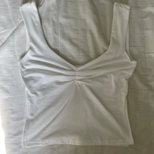 Vit croppad linnetopp med twistad front🤍 - Säljer en vit croppad linnetopp med breda axelband och snygg twistad detalj framtill! Toppen har djup v-ringning både fram och bak och är sydd i mjuk bomull✌🏼. Vet ej vilket märke, hör av dig om du har någon fundering!💭