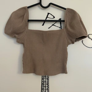 Beige ribbad topp med puffärm från H&M - Beige topp med ribbad struktur och puffiga korta ärmar från H&M i storlek XS. Modellen är croppad med fyrkantig urringning. Toppen är i mycket bra skick. 