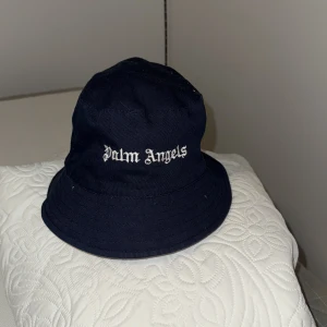 Palm Angels bucket hats i bomull - Två snygga bucket hats från Palm Angels, en i mörkblått och en i rött. Klassisk form med bred brätte och broderad logga framtill. Tillverkade i bomull, perfekta för att lyfta din streetwear-look.