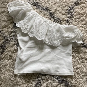Vit offshoulder topp med volang - Superfin vit topp med bred volang i broderad spets och offshoulder-design. Står att storleken är 152 men passar som en xs! Passar perfekt nu till sommaren