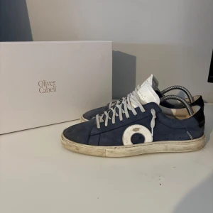 Blå sneakers från Oliver Cabell - Snygga sneakers från Oliver Cabell i marinblå mocka med vita detaljer och svart häl. Skorna har vit sula, rund tå och klassisk snörning. Perfekt för dig som gillar stilrena och trendiga sneakers med unik design.