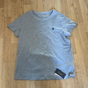 Grå t-shirt från Polo Ralph Lauren - Säljer en klassisk grå t-shirt från Polo Ralph Lauren med liten broderad logga på bröstet. T-shirten har rund hals och korta ärmar. Perfekt basic-plagg för garderoben. Passar s med. Nypris cirka 600 anvlnd några gånger 