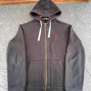 Svart hoodie från Polo Ralph Lauren - Svart hoodie från Polo Ralph Lauren med dragkedja. Sliten på baksidan av vänstra armen (bild 5), annars bra skick.