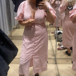 Ljusrosa broderad klänning med puffärm - Supersöt ljusrosa klänning med broderade detaljer och knappar framtill. Klänningen har v-ringning, puffiga korta ärmar och slits nertill. Perfekt för sommarens alla tillfällen och ger en romantisk vibe. Väldigt lik adoore klänningarna i modellen!! Den är använd max 3 gånger