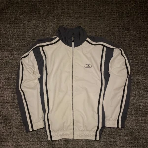 Vintage Adidas vindjacka  - Snygg vintage Adidas vind jacka i mycket bra skick.  Hängaren som man ser på bild 2 är trasig. Utöver det är den felfri. Kan du sy så är det en lätt fix. Mått 76x67 Stl ”L” men passar även M väldigt bra✌️ 