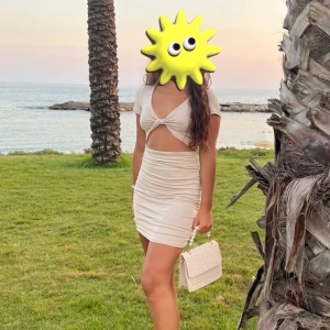 Beige omlott kortklänning - Säljer en beige kortklänning med omlott-detalj och snygg cut-out framtill. Klänningen har korta ärmar och är figurnära med rynkade sidor som ger en cool look. Perfekt för sommarkvällar vid stranden. Materialet känns mjukt och stretchigt.