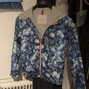 Moncler windbreaker - Snygg vindjacka från Moncler med blått och vitt blommönster, hel dragkedja och luva. Jackan har grått innerfoder och klassisk Moncler-logga på ärmen. Perfekt för dig som vill sticka ut med en unik och stilren jacka! Pris kan diskuteras. Hör av er!