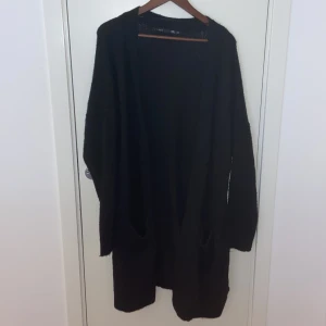 Svart lång kofta med fickor - Svart, lång och loose kofta från lager 157 med två stora fickor framtill. Koftan har lång ärm och är gjord i mjukt stickat material som känns skönt mot huden. Perfekt att slänga på sig när det är lite kyligt ute.