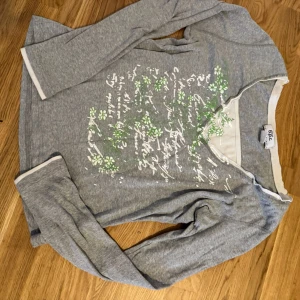 Grå långärmad tröja thriftat har använt den förra året nästan varje dag t skolan passar alla jag är 60kg  - Grå långärmad tröja från bpc med vit kant vid hals och ärmslut. Framsidan har ett tryck med vit text och gröna blommor som ger en chill och fräsch vibe. Mjuk bomullskänsla och relaxed passform, perfekt för dig som gillar casual stil.