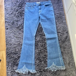 Blå bootcut jeans med fransar från Joy - Säljer ett par blå bootcut jeans från Joy Fashion Jeans med snygga fransar längst ner på benen. Jeansen har klassisk femficksdesign, normal passform och är tillverkade i jeansmaterial. Perfekt för dig som vill sticka ut med coola detaljer. Size 16, stretchiga jeans med jeans matrial, helt oandvända, e lite korta i storleken, om det behövs fråga om mer bilder på jeansen!