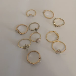 10-pack guldiga ringar - 10 st guldiga ringar med olika former och detaljer. Perfekt för dig som gillar att mixa och matcha flera ringar på samma hand för en cool och personlig stil. Materialet är zinc alloy + rhinestones + resin. (300)