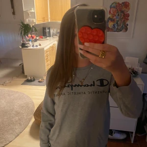 Grå sweatshirt från Champion - Säljer en grå långärmad sweatshirt från Champion i storlek Large. Tröjan har klassisk rund hals och tryckt logga framtill. Perfekt för chill dagar och enkel att matcha med jeans eller mjukisbyxor. Materialet är mjukt och skönt, troligtvis bomull och polyester.