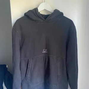 Svart hoodie från C.P. Company - Svart hoodie från C.P. Company. Skick 7/10, pga att den har krymt lite. Det är storlek S men den sitter som en XS. Hör av er vid frågor!